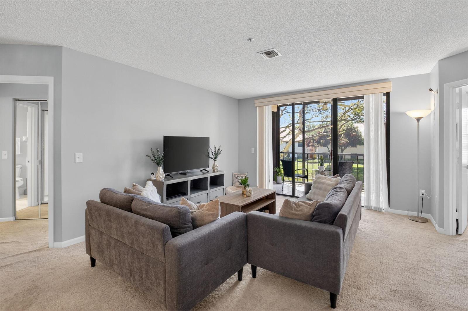 A living room features a gray sectional sofa, a television console, and a sliding glass door — 5155 Europa Drive # M, Boynton Beach FL 33437, BOYNTON BEACH, FL
