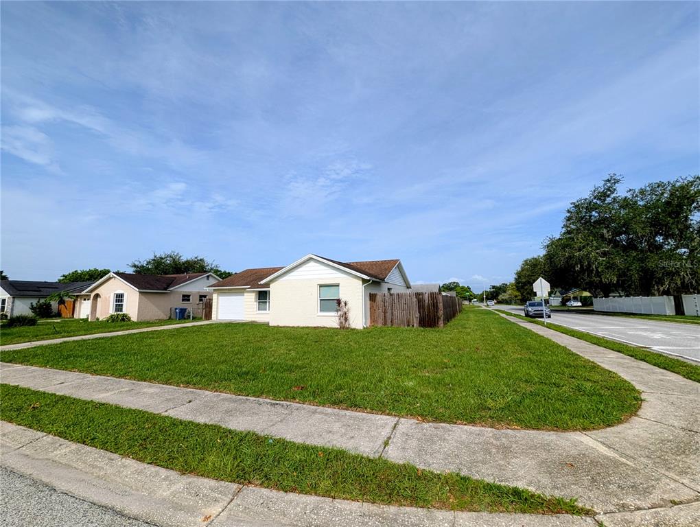 A single-story house with a white exterior, a garage, and a wooden fence on a corner lot — 3153 LODI DRIVE, NEW PORT RICHEY, FL