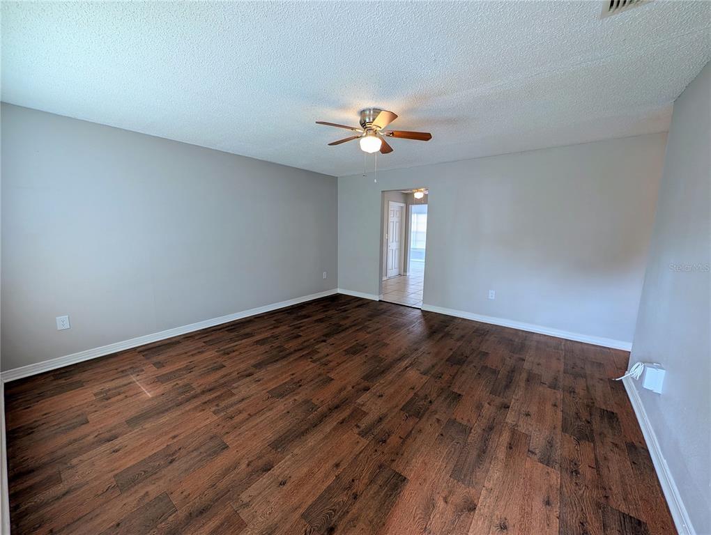 An empty room features gray walls, dark wood-look flooring, and a ceiling fan — 3153 LODI DRIVE, NEW PORT RICHEY, FL
