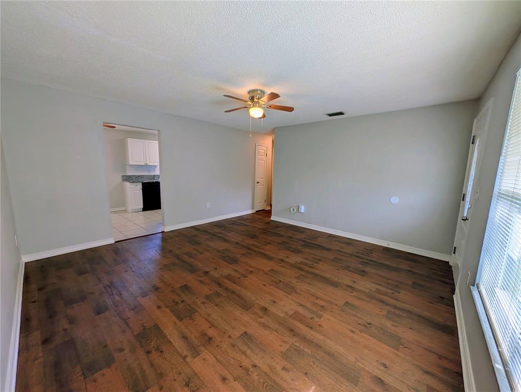 An empty living room with wood-look flooring, light gray walls, and a ceiling fan — 3153 LODI DRIVE, NEW PORT RICHEY, FL