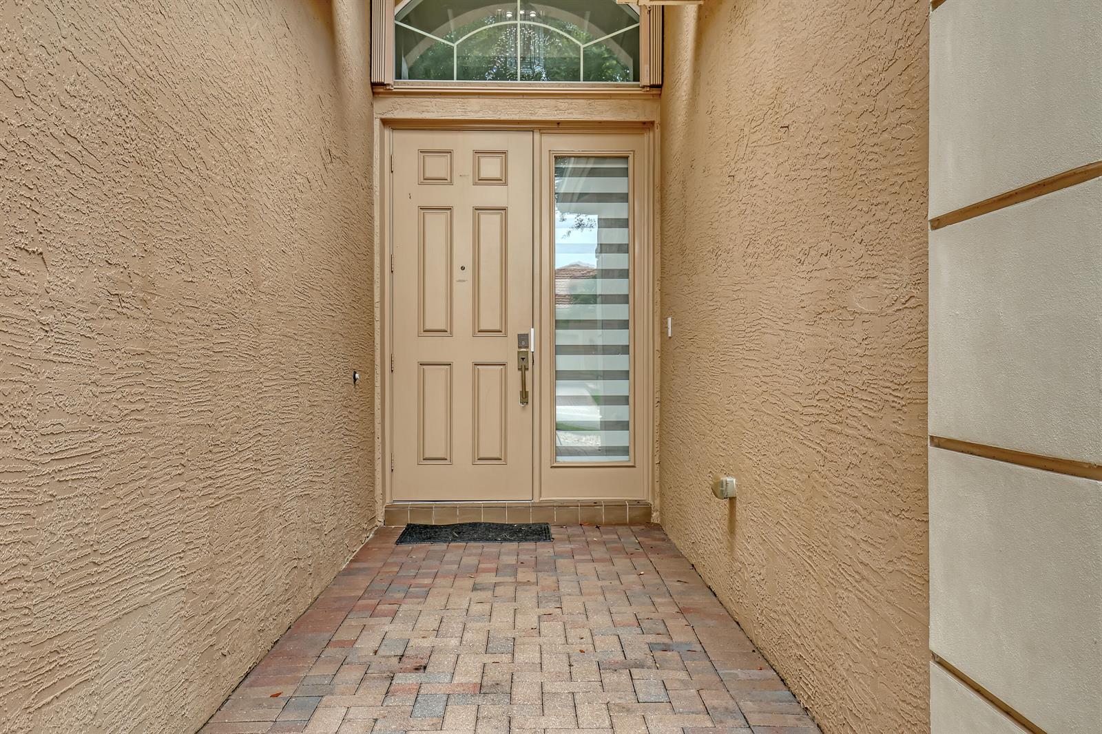 A tan front door with a sidelight and arched transom window sits at a paved entryway — 10673 Richfield Way, Boynton Beach FL 33437, BOYNTON BEACH, FL