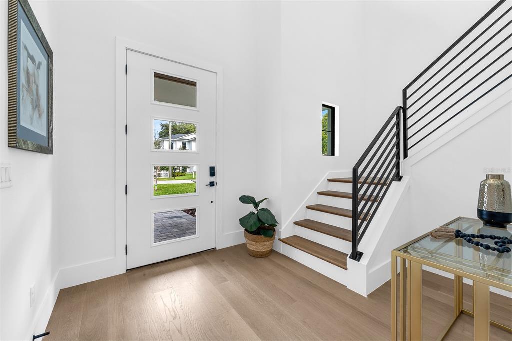 A bright entryway features light wood floors, a modern white door, and a black-railed staircase — 1546 MILLER AVENUE, WINTER PARK, FL