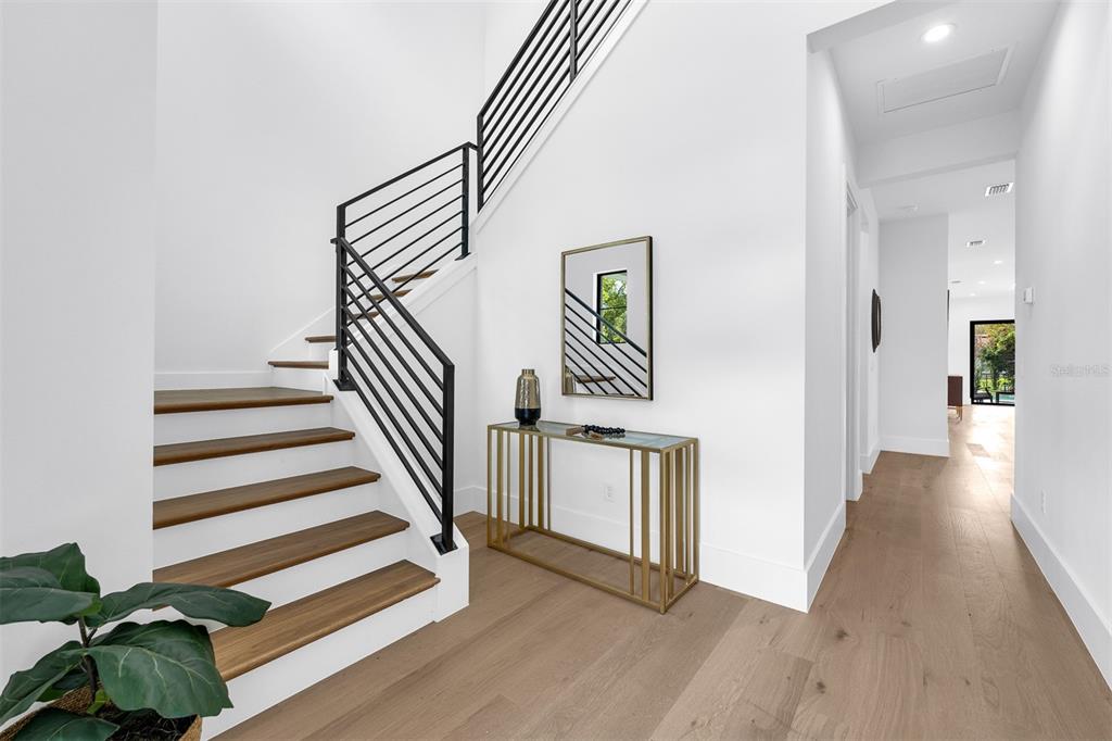 A modern entryway features a wooden staircase with black railings, a gold console table, and hardwood floors — 1546 MILLER AVENUE, WINTER PARK, FL