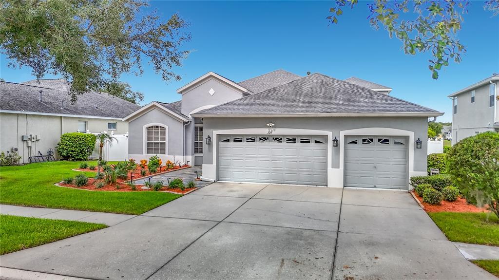 A gray single-story house features a three-car garage, a concrete driveway, and landscaped front beds — 220 RONJA LANE, VALRICO, FL