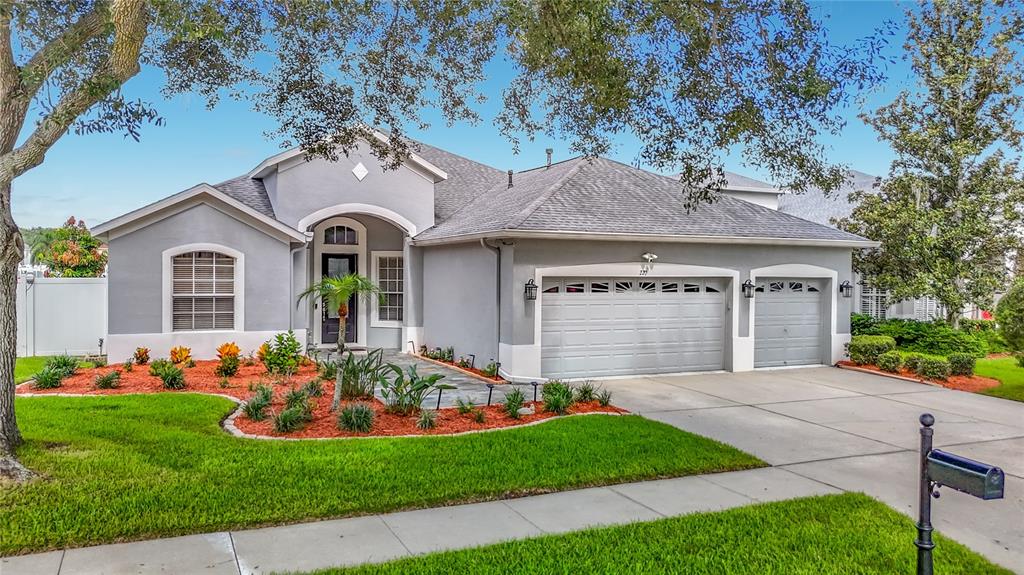 A single-story gray house with a three-car garage and landscaped front yard — 220 RONJA LANE, VALRICO, FL