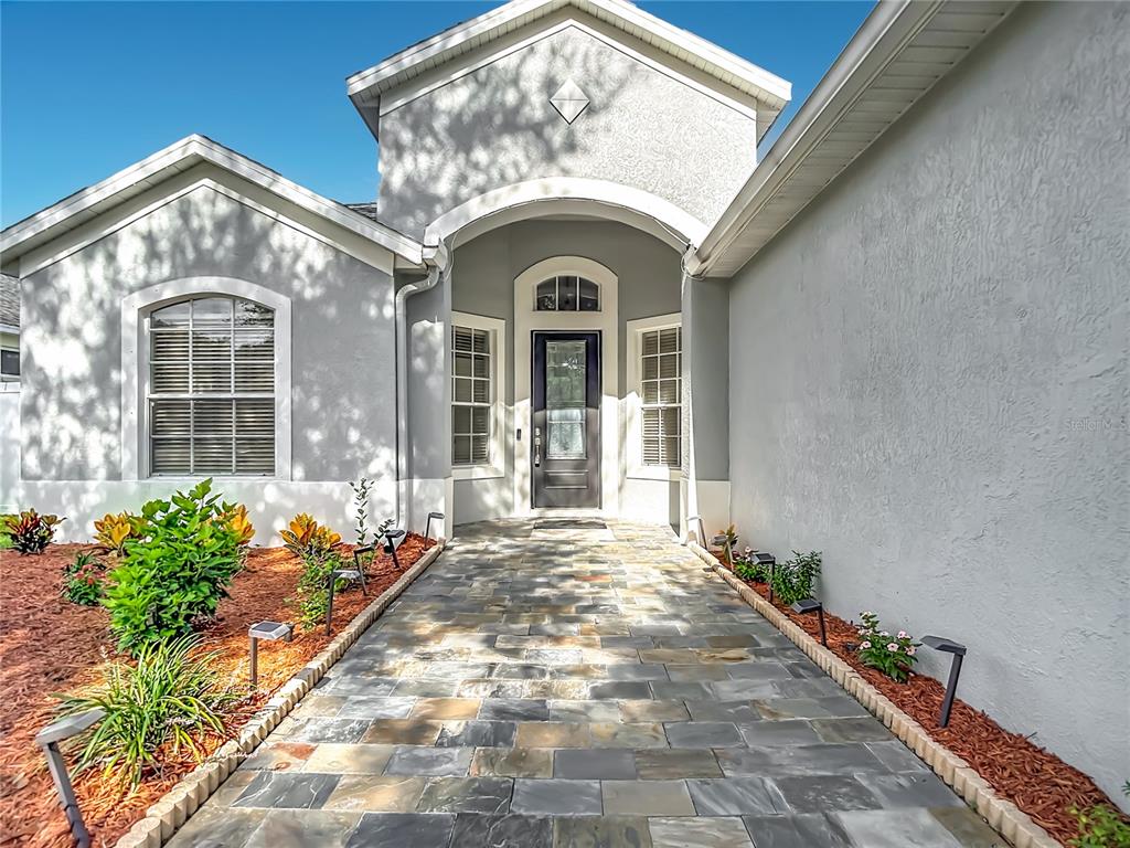 A stone walkway leads to the front entrance of a gray house with arched architectural details — 220 RONJA LANE, VALRICO, FL