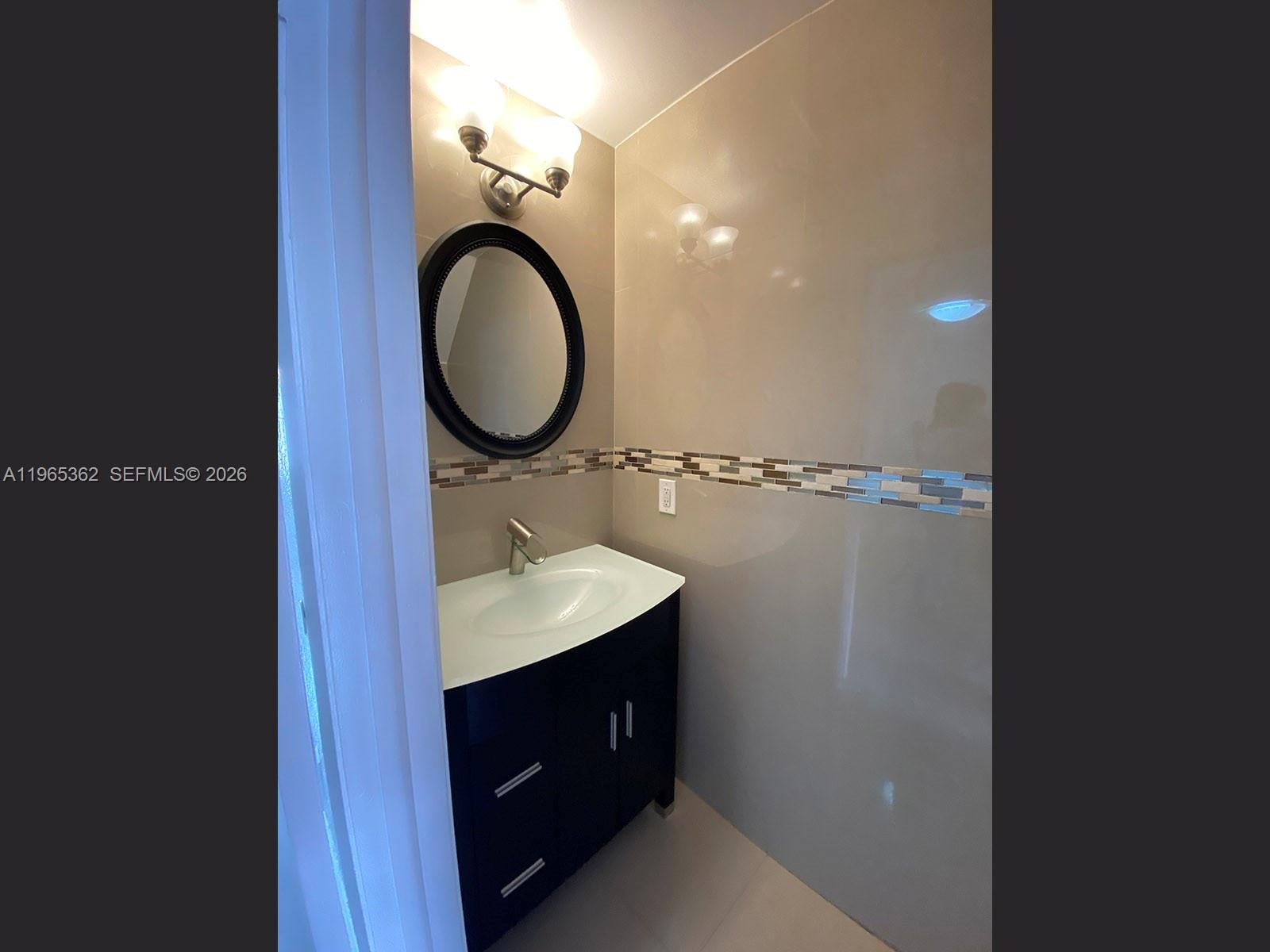 A bathroom features a dark vanity, a round mirror, and a decorative tile backsplash — 8031 NW 8th St # 17, Miami FL 33126, MIAMI, FL