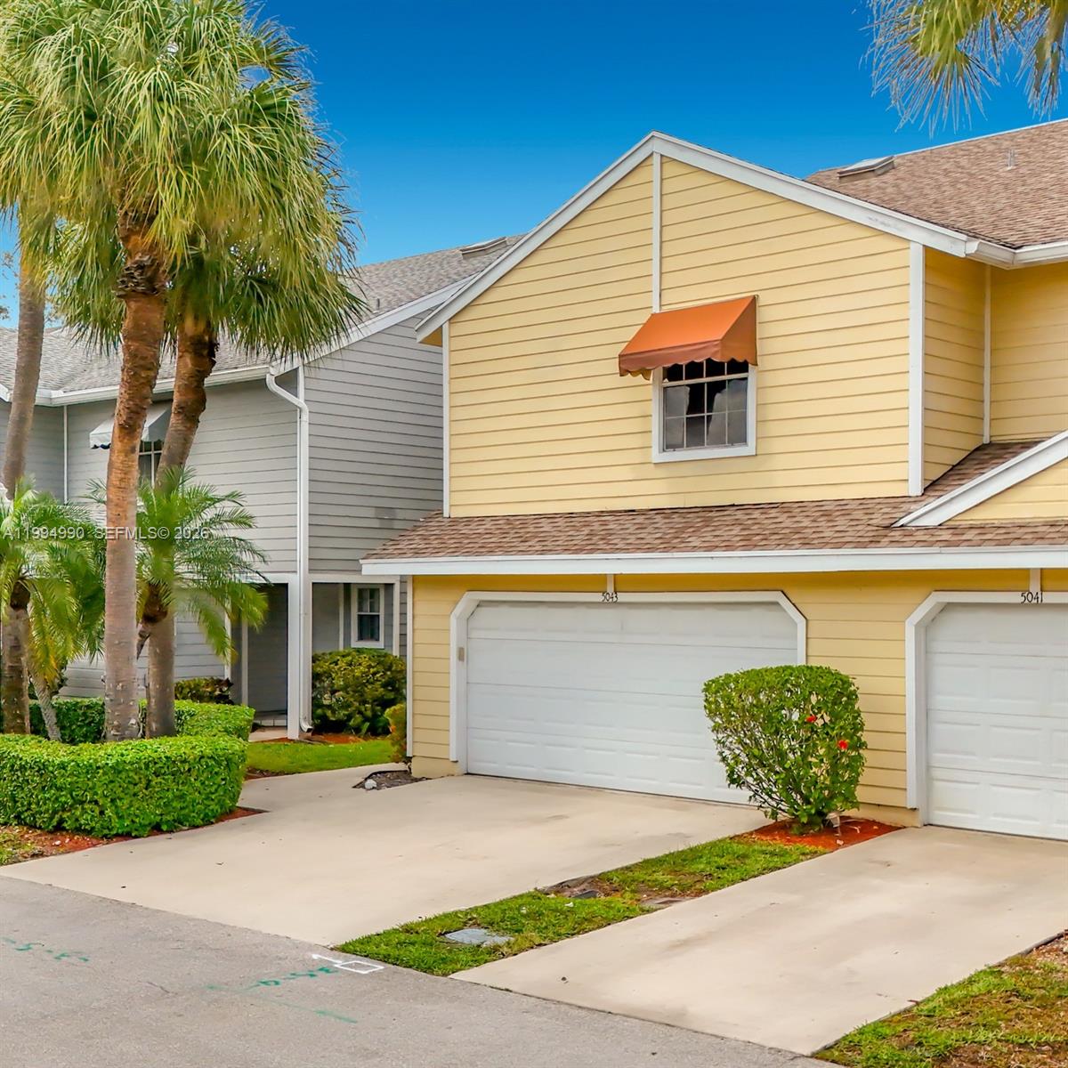 A yellow two-story townhouse with a white garage door and a small orange window awning — 5043 Pointe Emerald Ln, Boca Raton FL 33486, BOCA RATON, FL