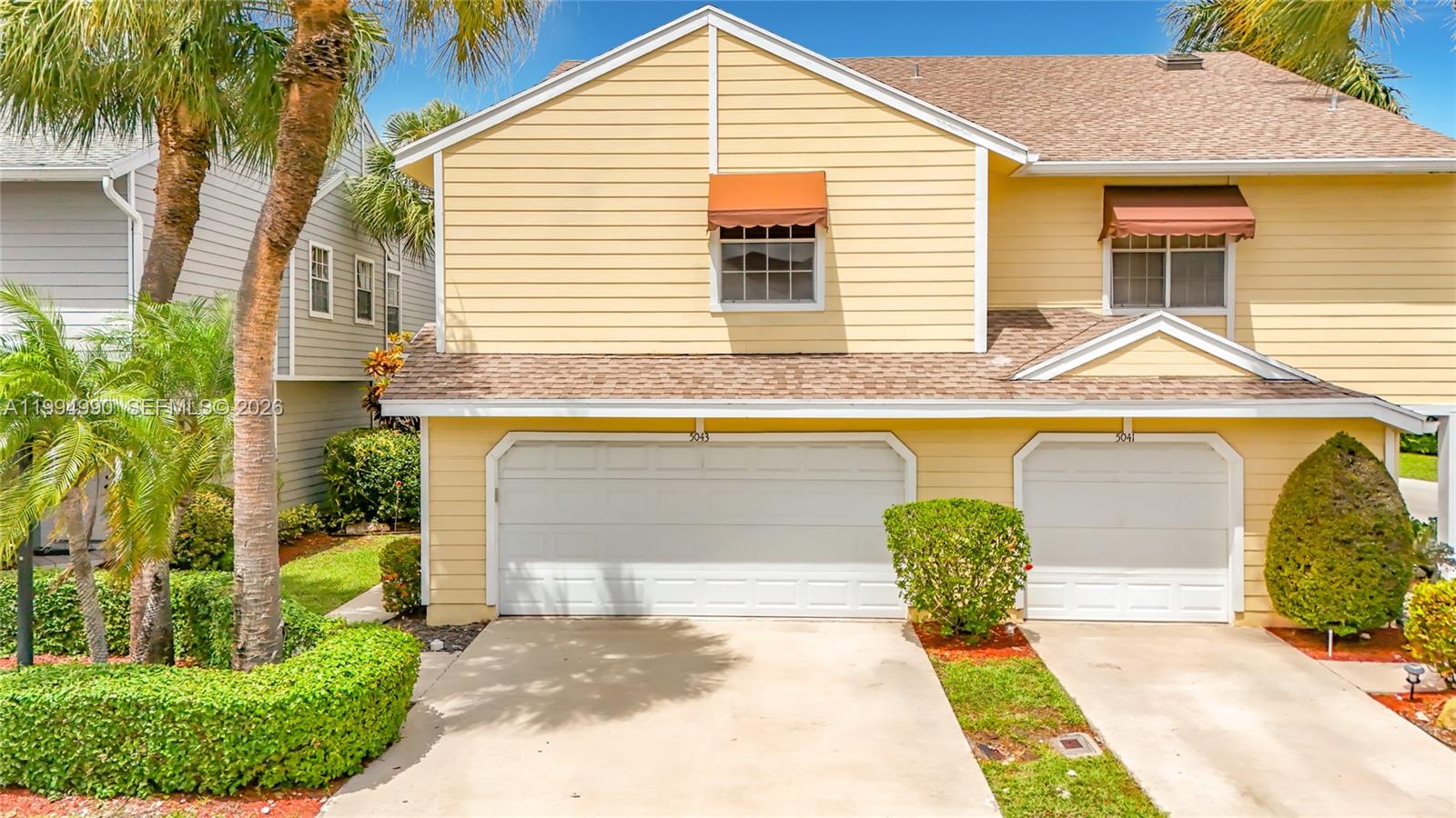 A yellow two-story townhouse features two white garage doors and brown fabric window awnings — 5043 Pointe Emerald Ln, Boca Raton FL 33486, BOCA RATON, FL