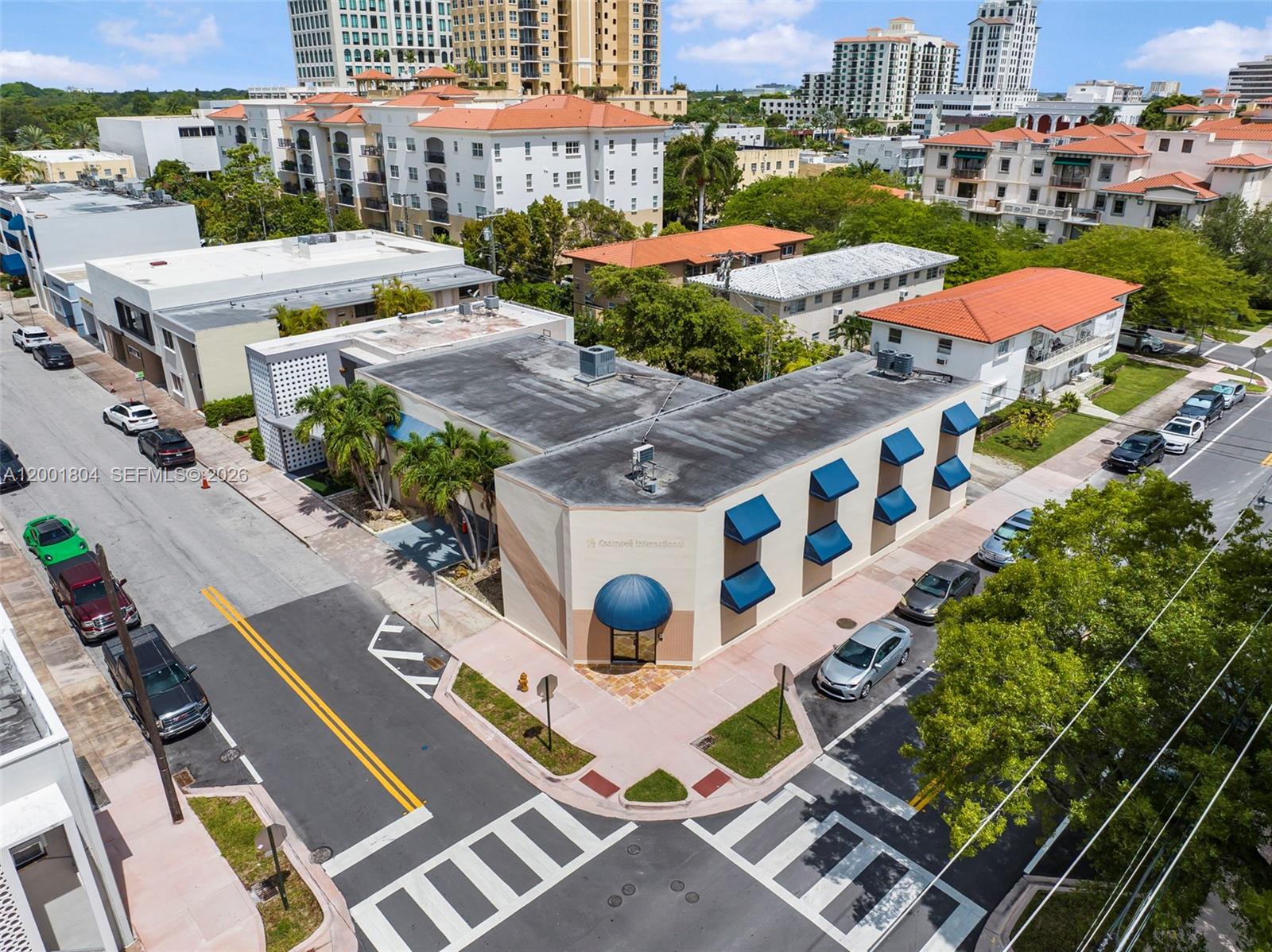 An aerial view shows a corner commercial building with blue awnings and surrounding street parking — 101 Madeira Ave, Coral Gables FL 33134, CORAL GABLES, FL
