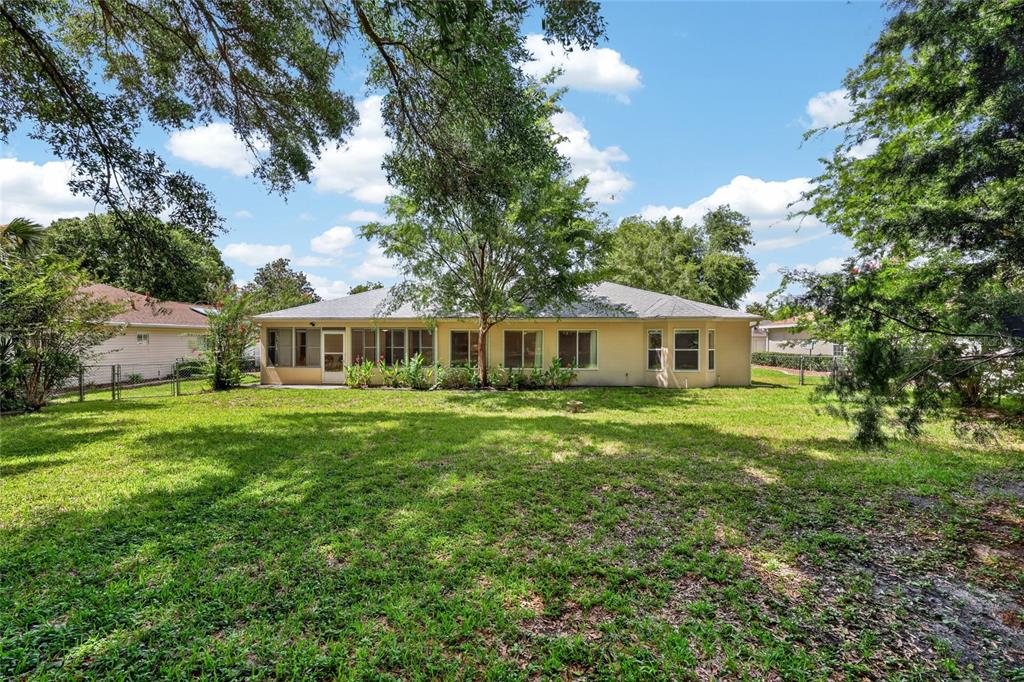 The backyard of a single-story house features a screened-in porch and mature trees — 11268 SW 139TH PLACE, DUNNELLON, FL
