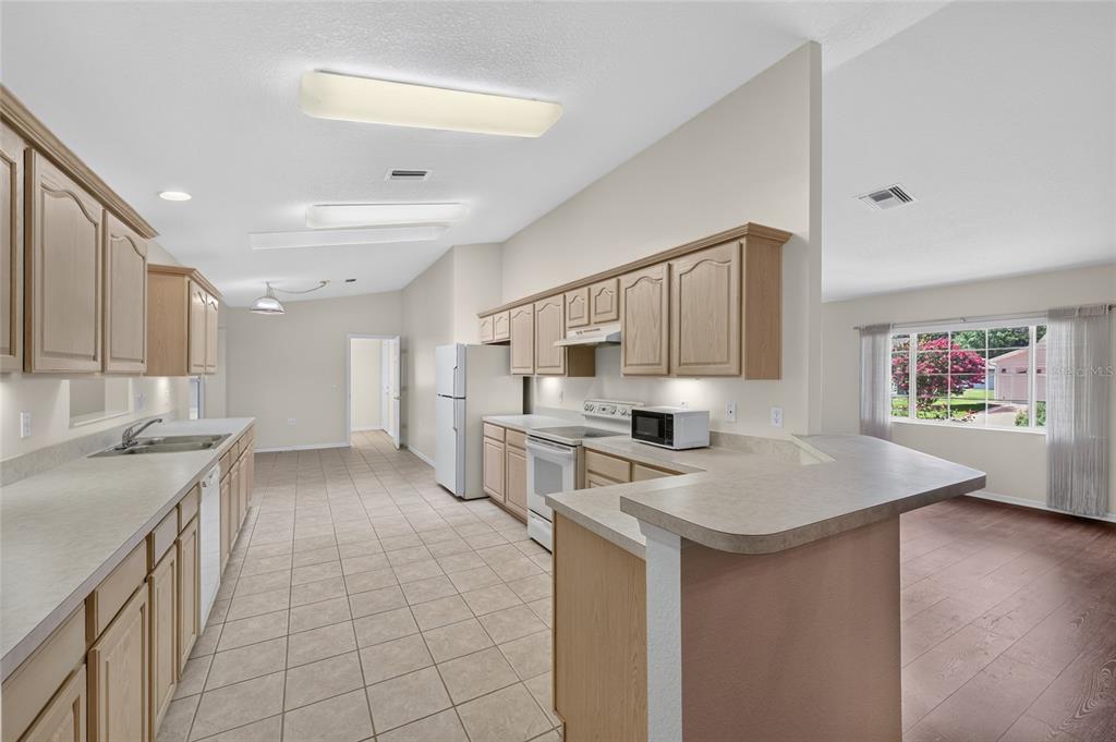 A kitchen with light wood cabinets, laminate countertops, and tile flooring, adjacent to a living area — 11268 SW 139TH PLACE, DUNNELLON, FL