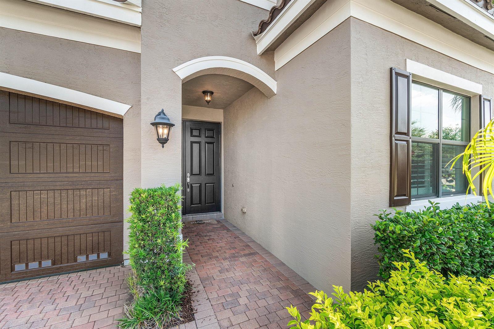 A brick walkway leads to a black front door under a covered entryway — 8109 Snowflake Obsidian Trail, Delray Beach FL 33446, DELRAY BEACH, FL