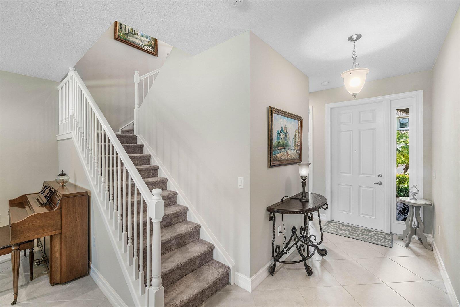 A foyer features a carpeted staircase, a piano, a console table, and a white front door — 8109 Snowflake Obsidian Trail, Delray Beach FL 33446, DELRAY BEACH, FL