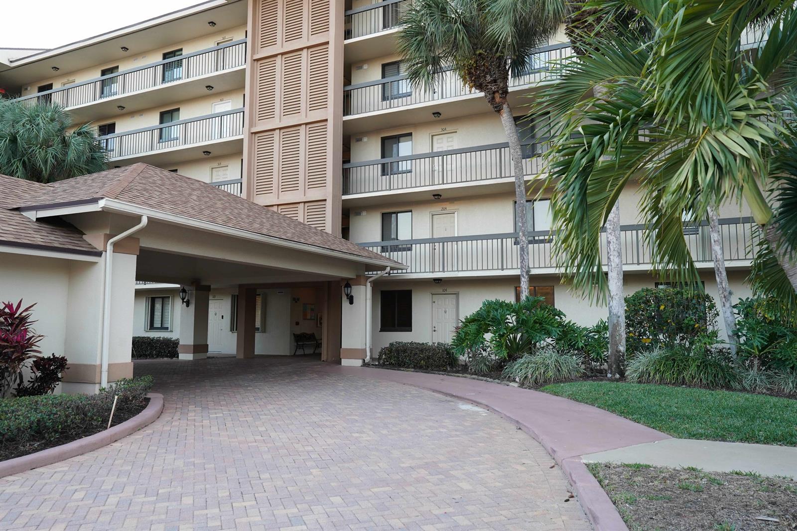 A paved driveway leads to the covered entrance of a multi-story apartment building with balconies — 2101 Marina Isle Way # 104, Jupiter FL 33477, JUPITER, FL
