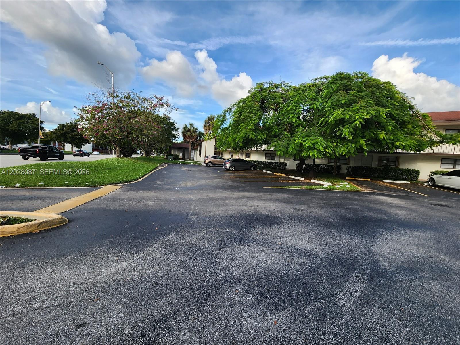 An outdoor parking lot features a large tree, green grass, and several parked cars — 461 NW 107 Ave # 102, Miami FL 33172, MIAMI, FL