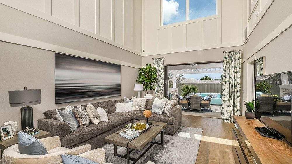 A high-ceilinged living room features a sectional sofa, coffee table, and sliding doors to a patio — 7012 FOXBORO WAY, NOKOMIS, FL