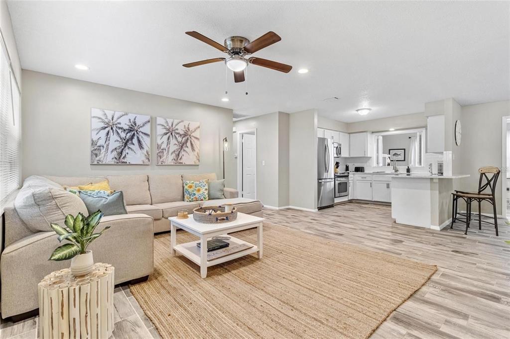 An open-concept living room and kitchen featuring a beige sectional, area rug, and wood-look flooring — 4904 19TH AVENUE W, BRADENTON, FL
