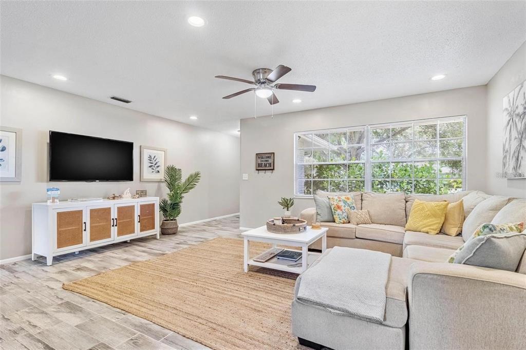 A living room features a sectional sofa, a television on a cabinet, and wood-look flooring — 4904 19TH AVENUE W, BRADENTON, FL