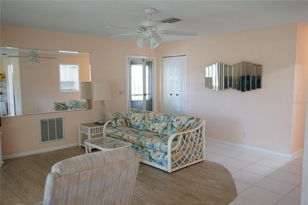 A living room features a floral sofa, light-colored walls, tile flooring, and a ceiling fan — 1901 CANTERBURY LANE UNIT 4, SUN CITY CENTER, FL