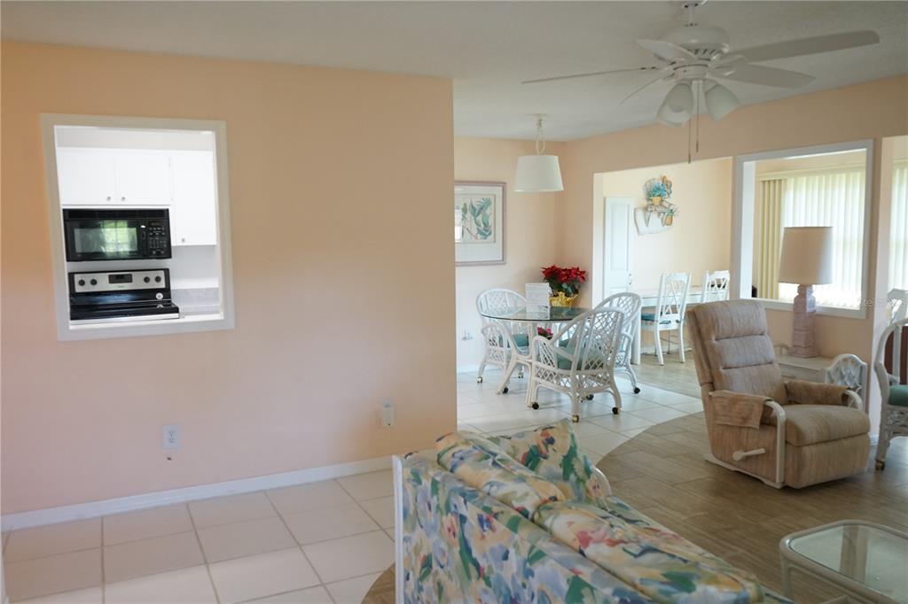 A living room with tile flooring, a floral sofa, and a view into the kitchen — 1901 CANTERBURY LANE UNIT 4, SUN CITY CENTER, FL