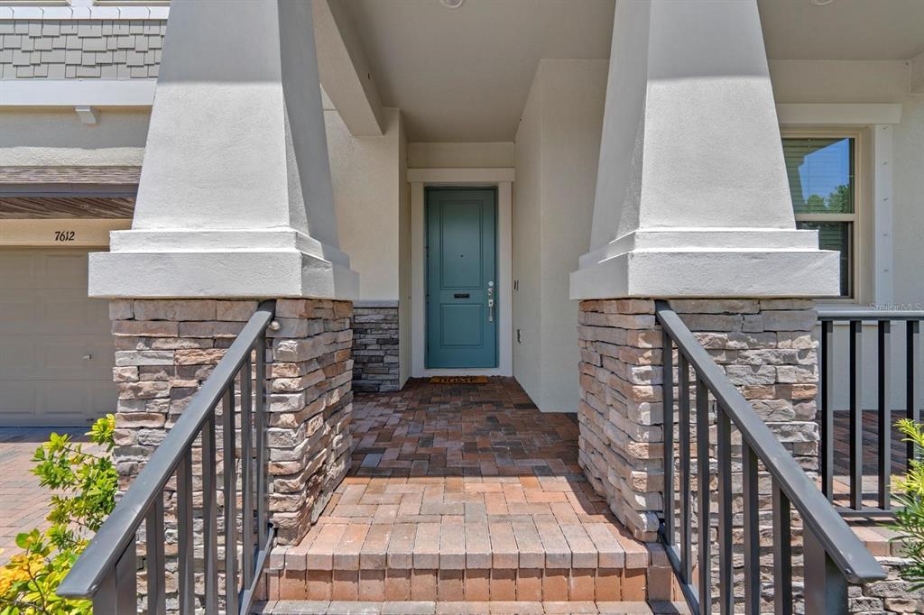 A front entryway features a teal door, stone-based pillars, and brick steps with metal railings — 7612 S JUANITA STREET, TAMPA, FL