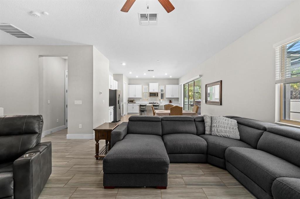 A living room with a gray sectional sofa opens to a kitchen with white cabinetry — 7612 S JUANITA STREET, TAMPA, FL