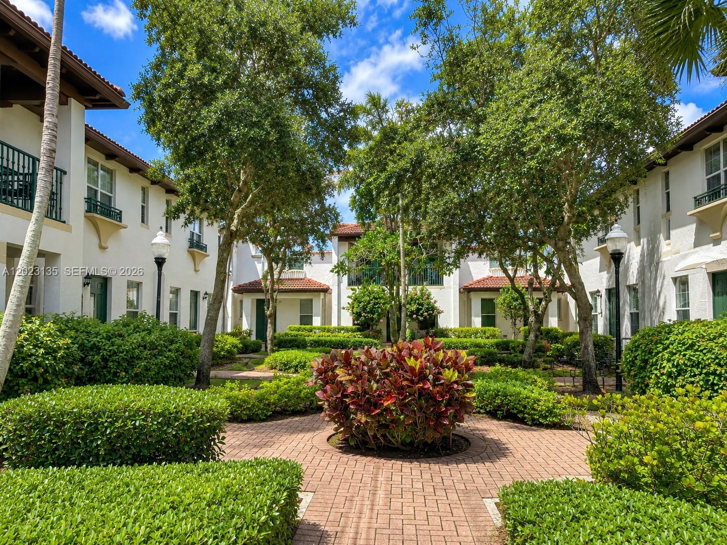 A brick courtyard with manicured hedges and trees sits between two-story white stucco buildings — 11837 SW 27th St, Miramar FL 33025, MIRAMAR, FL