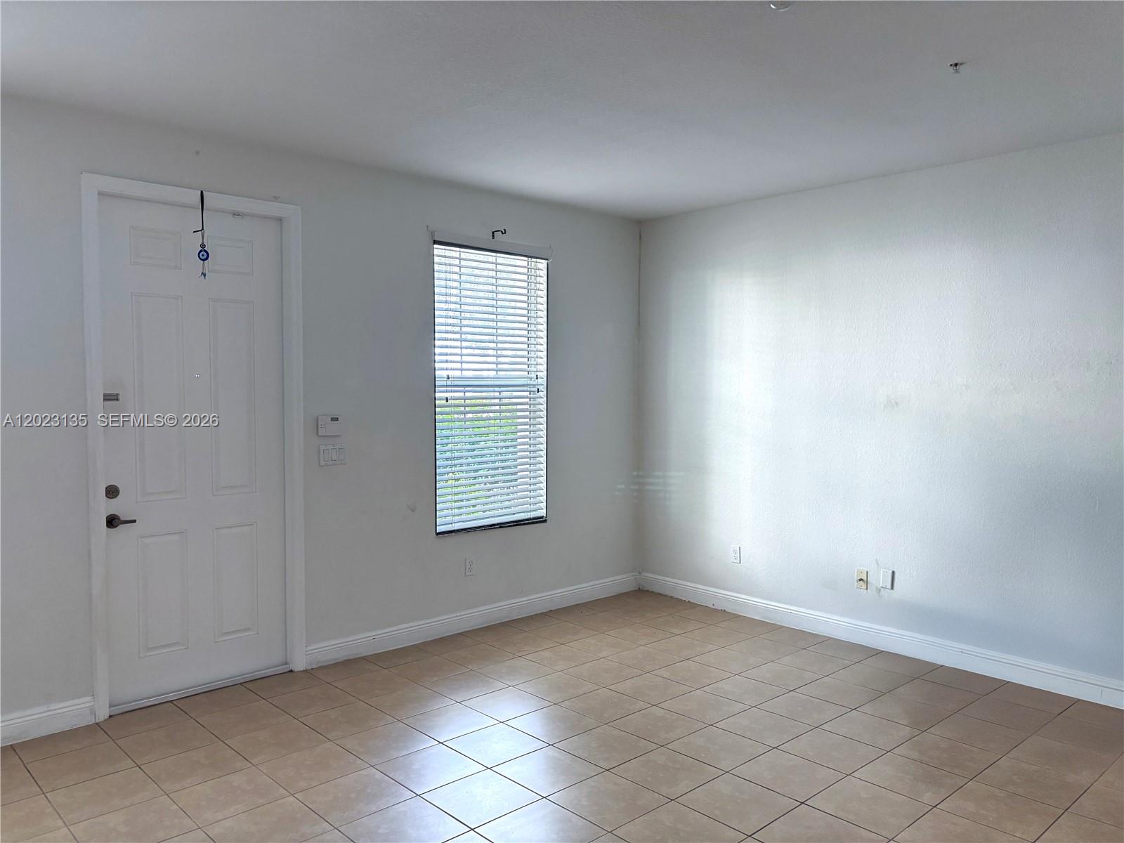 An empty room features white walls, tiled flooring, a single window with blinds, and a door — 11837 SW 27th St, Miramar FL 33025, MIRAMAR, FL