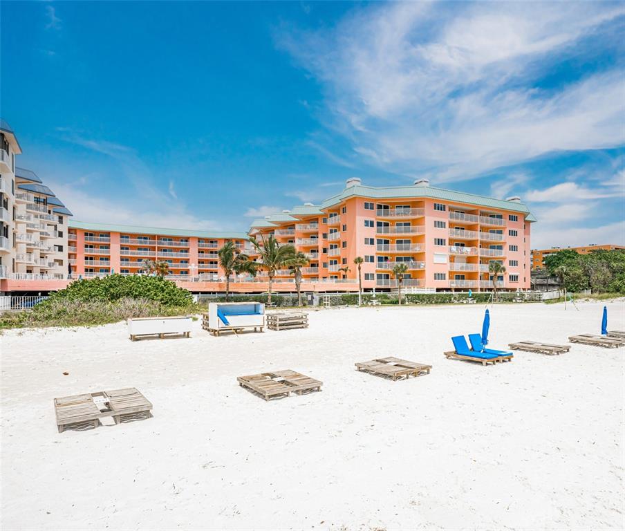A multi-story peach-colored resort building sits behind a sandy beach with wooden platforms — 18400 GULF BOULEVARD UNIT 2405, INDIAN SHORES, FL