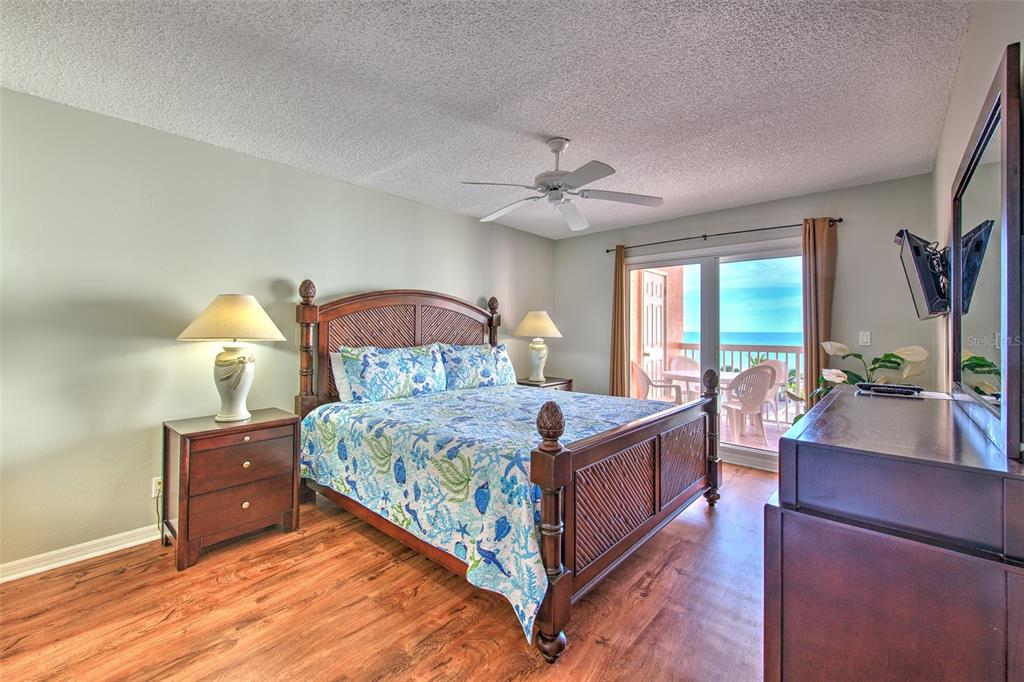 A bedroom with a wooden bed, patterned bedding, and a balcony overlooking the ocean — 18400 GULF BOULEVARD UNIT 2405, INDIAN SHORES, FL