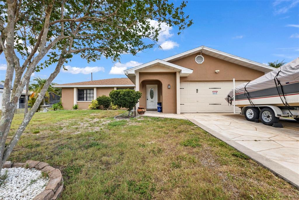 A tan single-story house with a white garage door and a boat parked in the driveway — 19519 MIDWAY BOULEVARD, PORT CHARLOTTE, FL