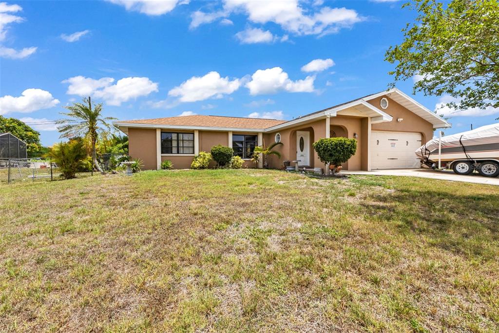 A single-story tan house with a brown roof, a two-car garage, and a boat trailer — 19519 MIDWAY BOULEVARD, PORT CHARLOTTE, FL