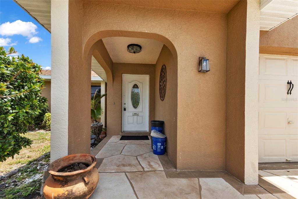 A covered entryway features a white front door, stone-look flooring, and a tan stucco exterior — 19519 MIDWAY BOULEVARD, PORT CHARLOTTE, FL