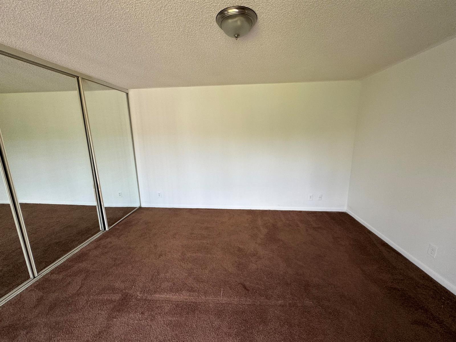 An empty bedroom features brown carpet, white walls, and mirrored sliding closet doors — 4664 Cherry Road, West Palm Beach FL 33417, WEST PALM BEACH, FL