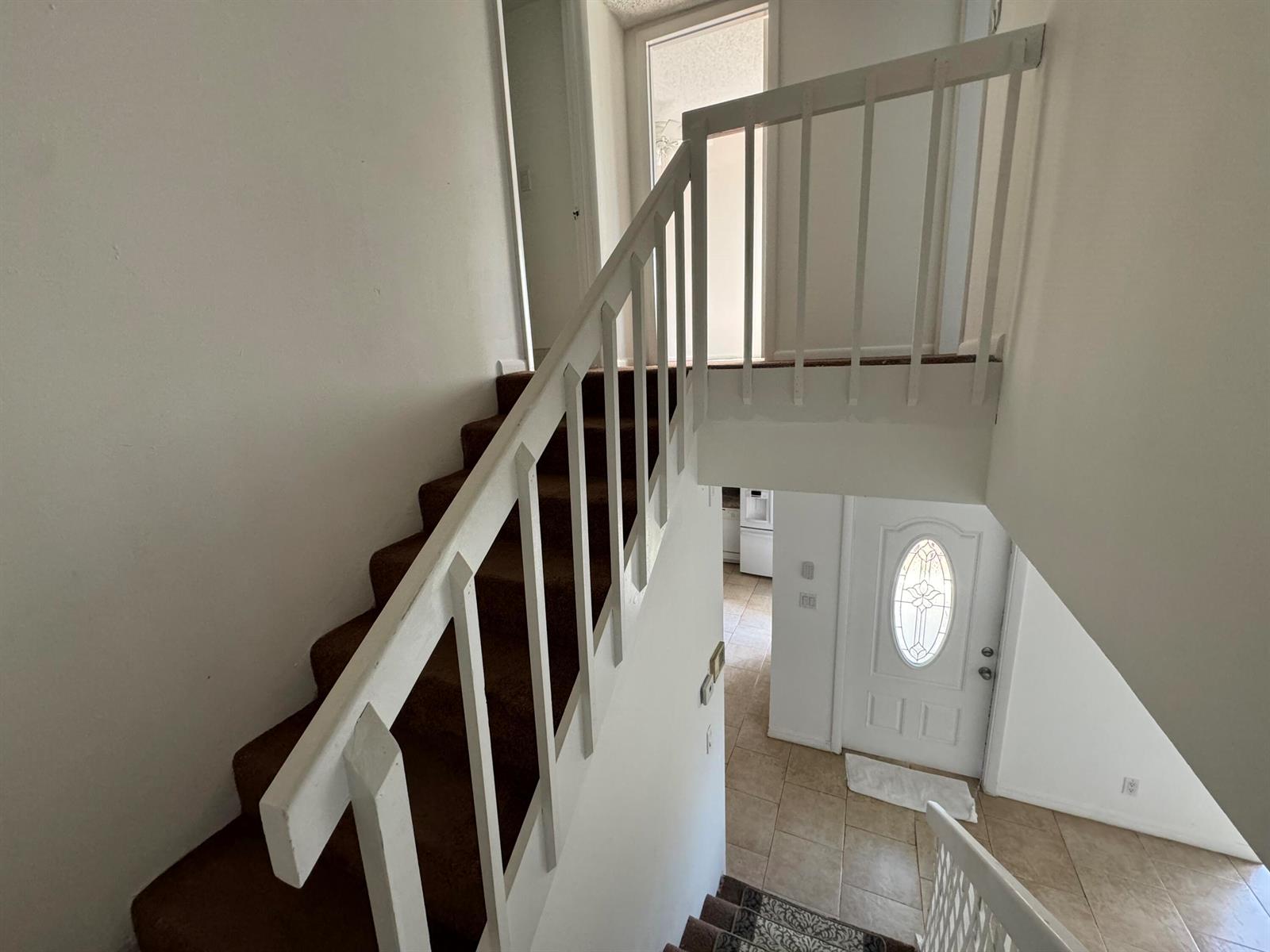 A staircase with brown carpet and white railings leads down to a tiled entryway — 4664 Cherry Road, West Palm Beach FL 33417, WEST PALM BEACH, FL