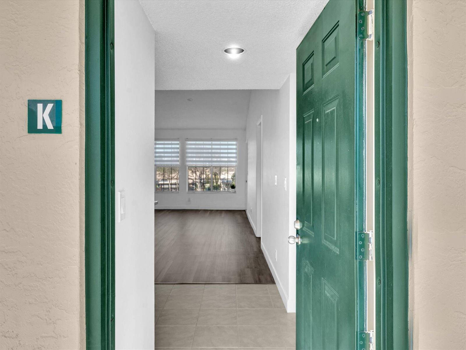 A view through an open green door into an apartment with tile and wood flooring — 6284 La Costa Drive # K, Boca Raton FL 33433, BOCA RATON, FL