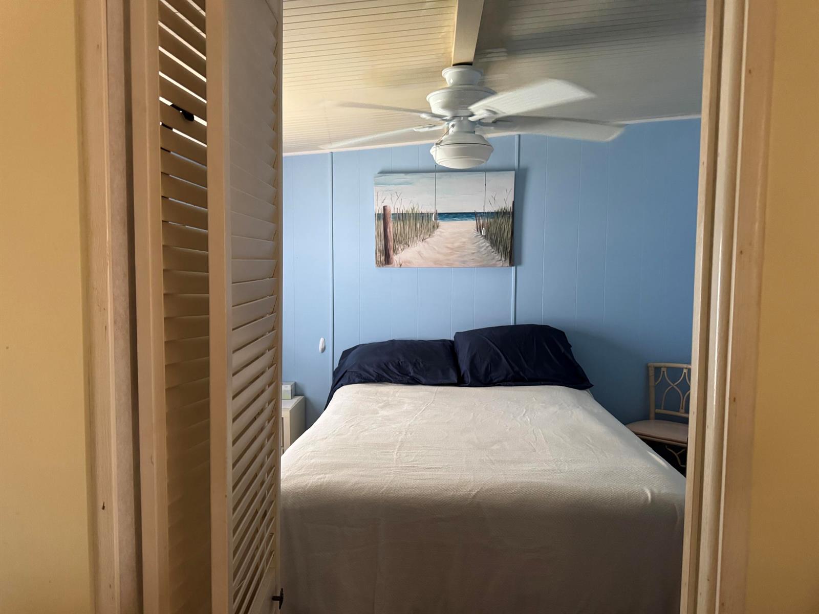 A bedroom with light blue walls, a white ceiling fan, and a beach-themed wall painting — 6658 SE 56th Lane, Okeechobee FL 34974, OKEECHOBEE, FL