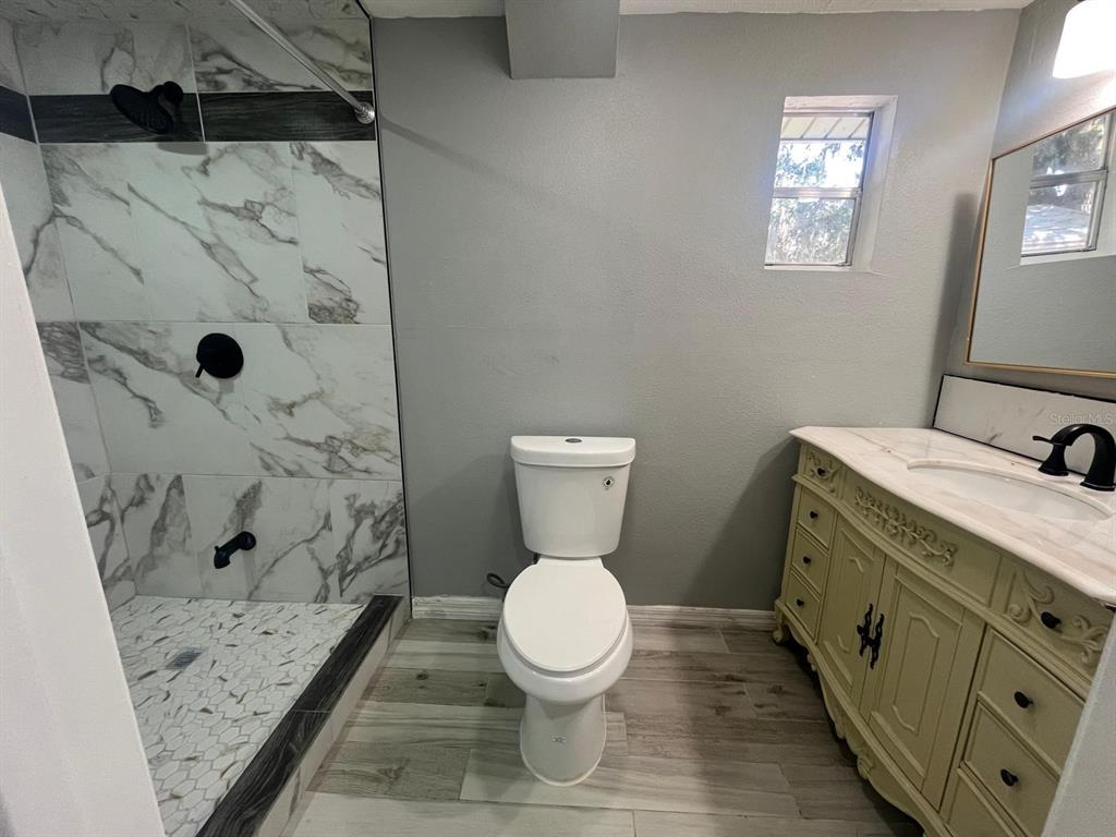 A bathroom features a marble-tiled shower, a white toilet, and a vintage-style vanity — 1400 DAKOTA AVENUE, ST CLOUD, FL