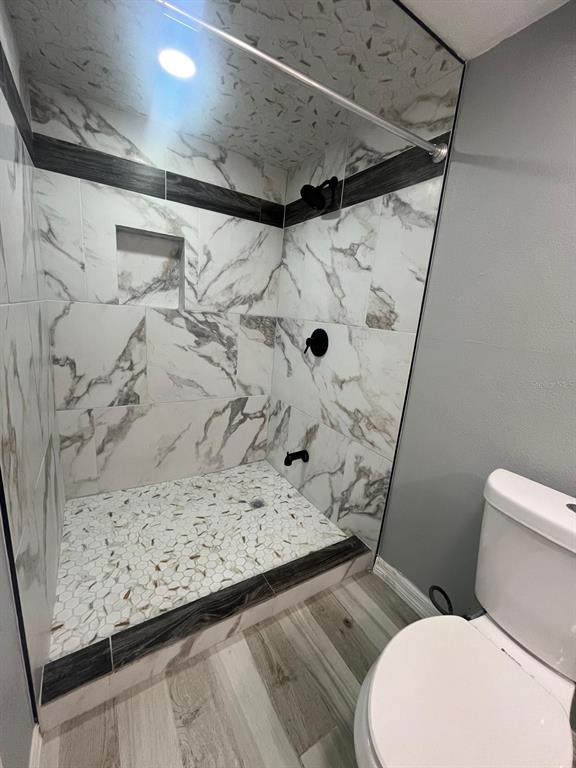 A bathroom features a walk-in shower with marble-look tile, a pebble floor, and black fixtures — 1400 DAKOTA AVENUE, ST CLOUD, FL