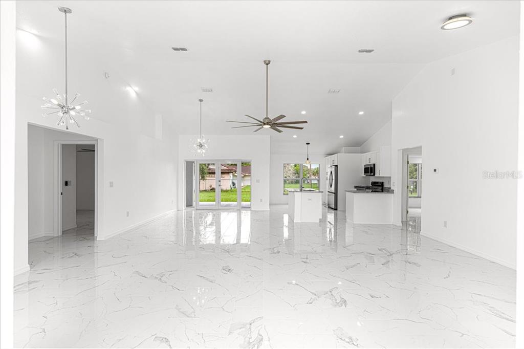An open-concept living and kitchen area features white marble-look tile floors and vaulted ceilings — 3625 SE 138TH STREET, SUMMERFIELD, FL