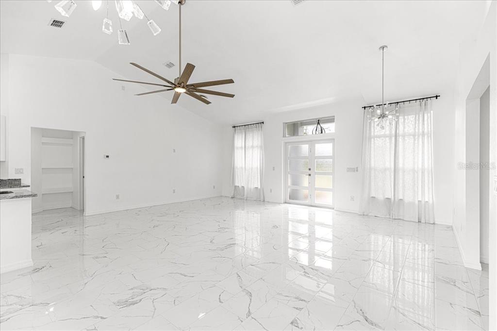 A bright, open-concept living room features white marble-look tile flooring and a vaulted ceiling — 3625 SE 138TH STREET, SUMMERFIELD, FL