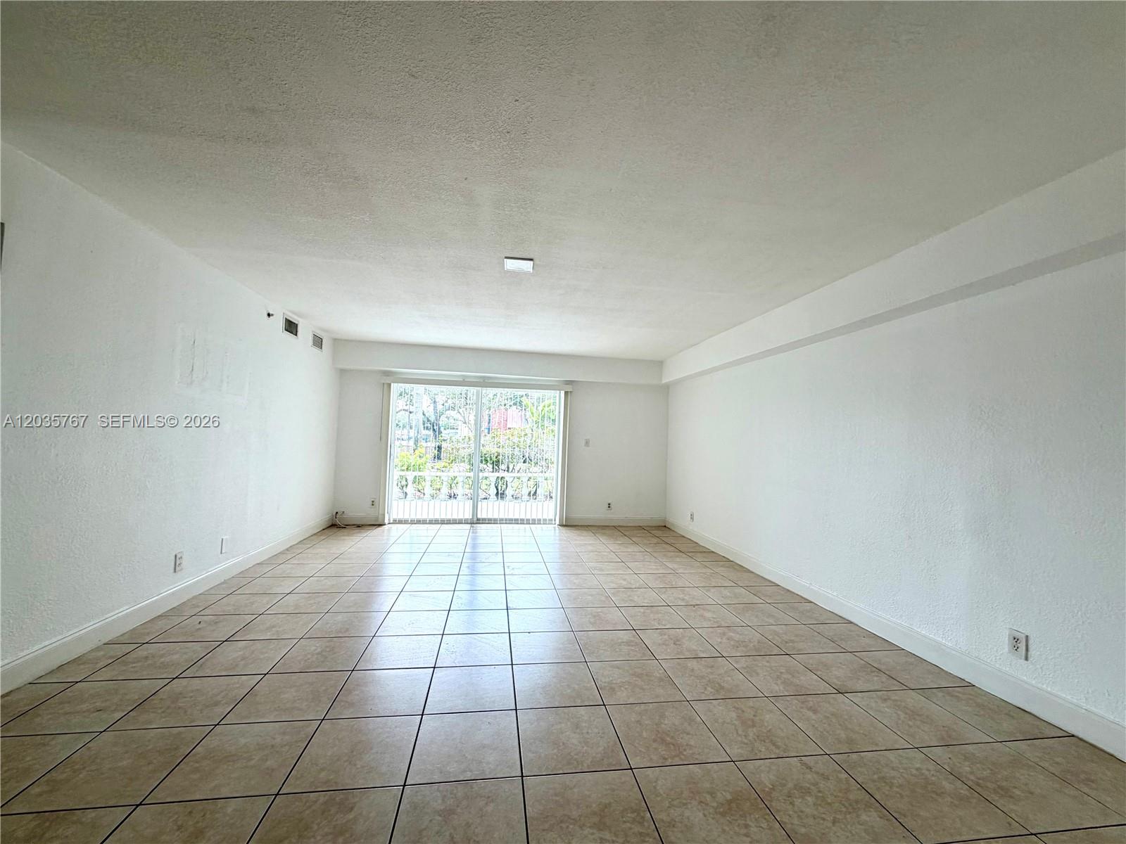 An empty living room features white walls, beige tile flooring, and sliding glass balcony doors — 4271 NW 5th St # 128, Plantation FL 33317, PLANTATION, FL