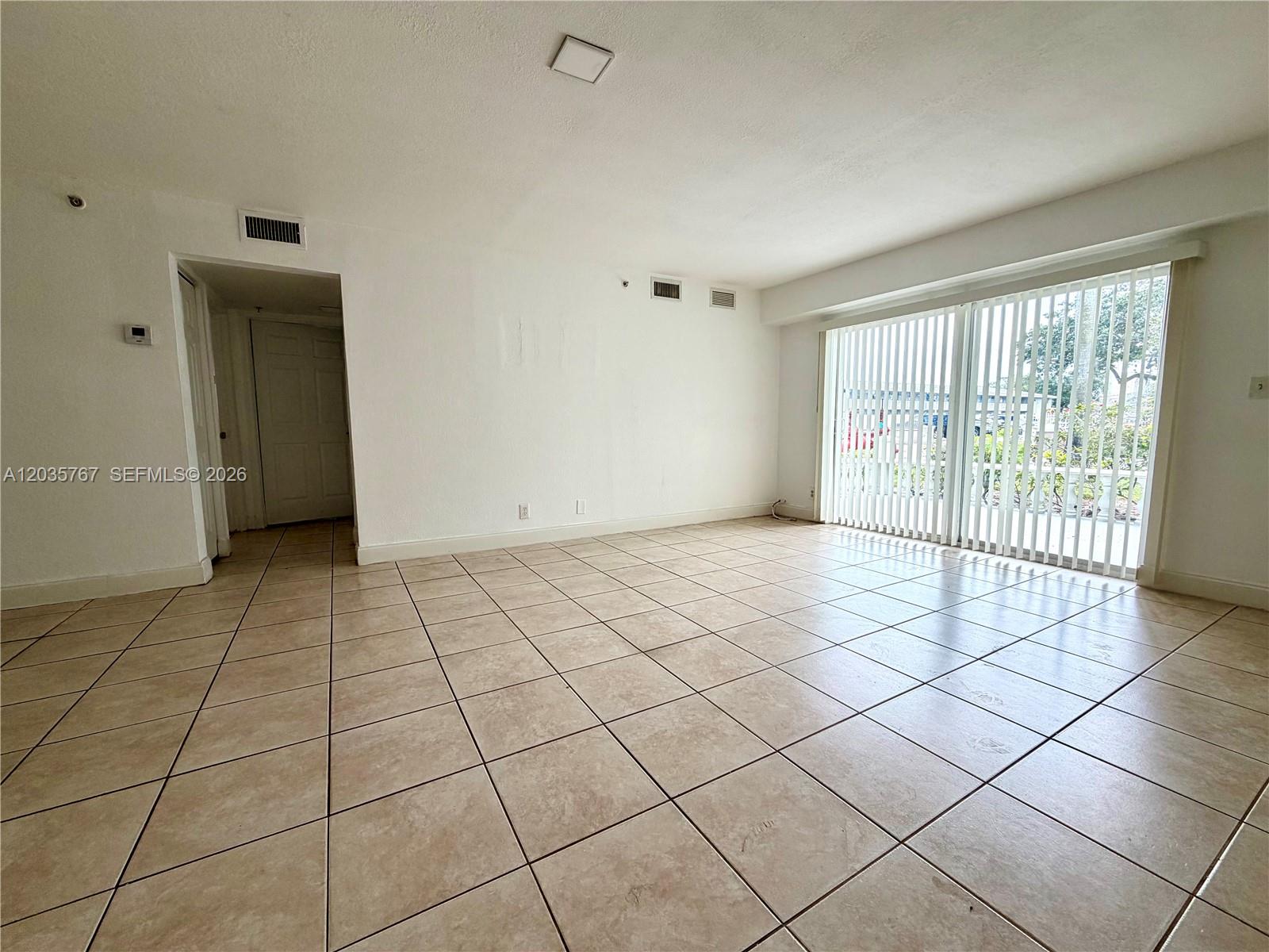 An empty room features beige tile flooring, white walls, and a large sliding glass door — 4271 NW 5th St # 128, Plantation FL 33317, PLANTATION, FL