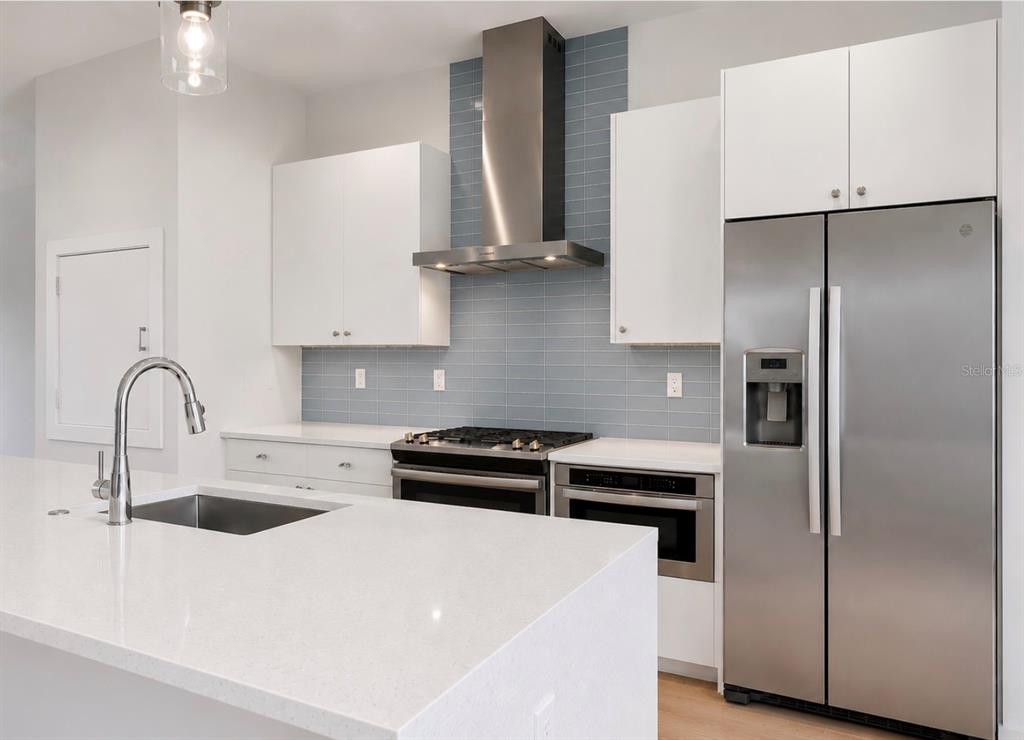 A modern kitchen features white cabinets, stainless steel appliances, a quartz island, and blue backsplash tile — 532 W PLAZA PLACE UNIT 3, TAMPA, FL
