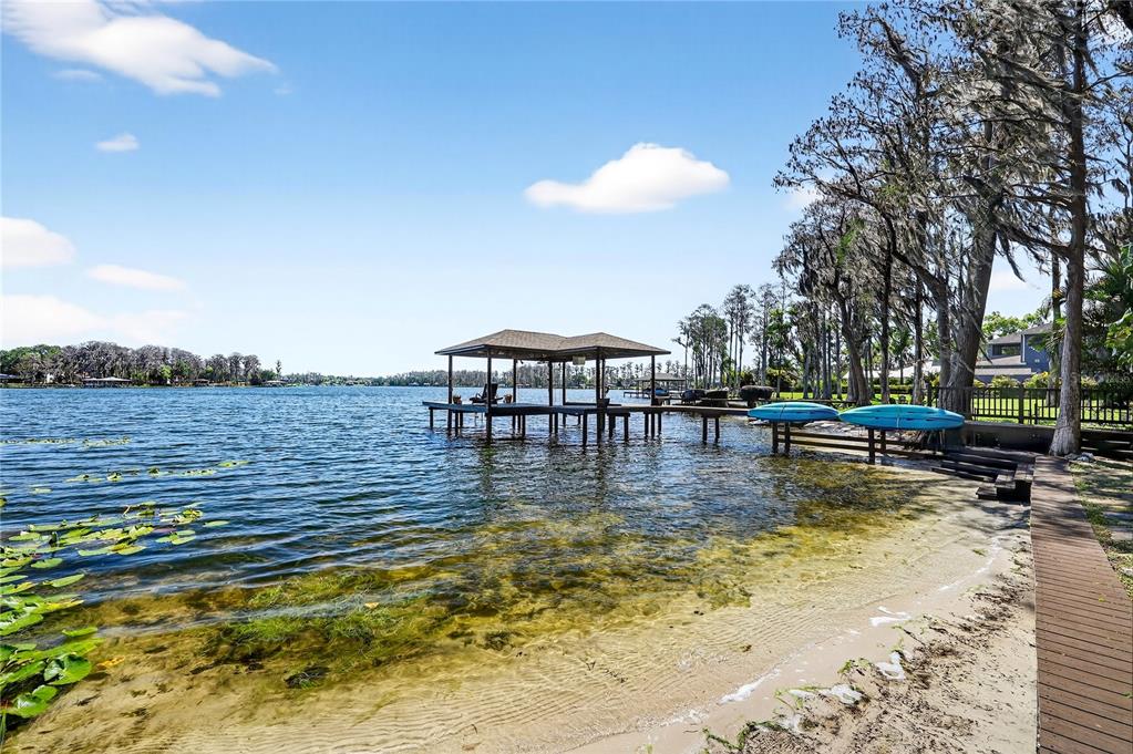 A wooden dock with a covered boat slip extends into a lake from a sandy shore — 19801 GUNN HIGHWAY, ODESSA, FL