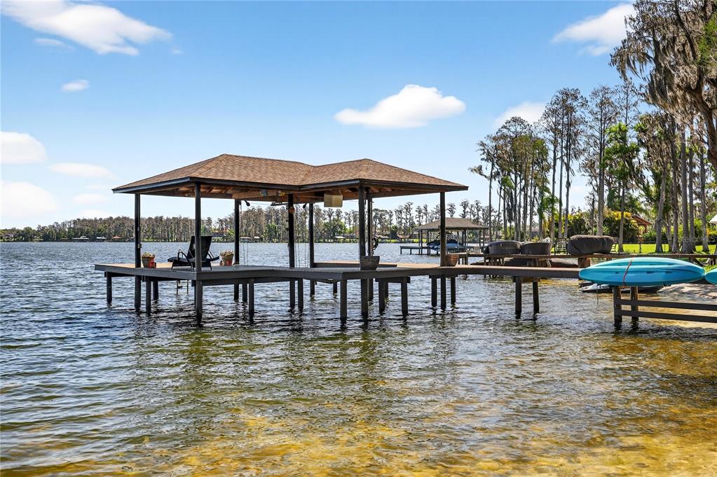 A wooden boat dock with a covered seating area extends into a calm lake — 19801 GUNN HIGHWAY, ODESSA, FL