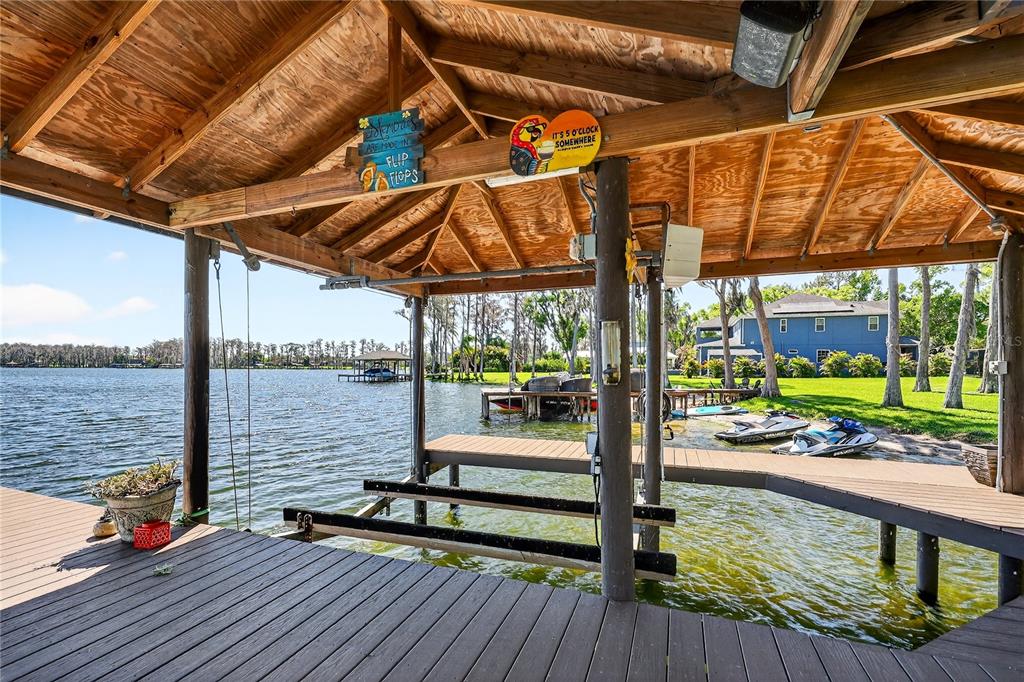 A covered wooden boat dock overlooks a lake with jet skis parked nearby — 19801 GUNN HIGHWAY, ODESSA, FL