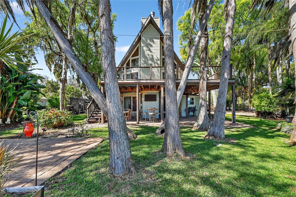 A two-story A-frame house with a wooden deck overlooks a grassy backyard with trees — 19801 GUNN HIGHWAY, ODESSA, FL