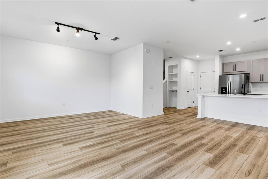 An open-concept living area features light wood-look flooring, white walls, and a modern kitchen — 9844 WALKWAY DRIVE, ORLANDO, FL